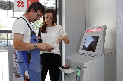 Ein Mann am Geldautomat. Eine Assistentin begleitet ihn